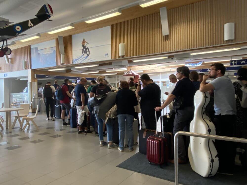 A group of people queuing at airport check in, many holding musical instrument cases